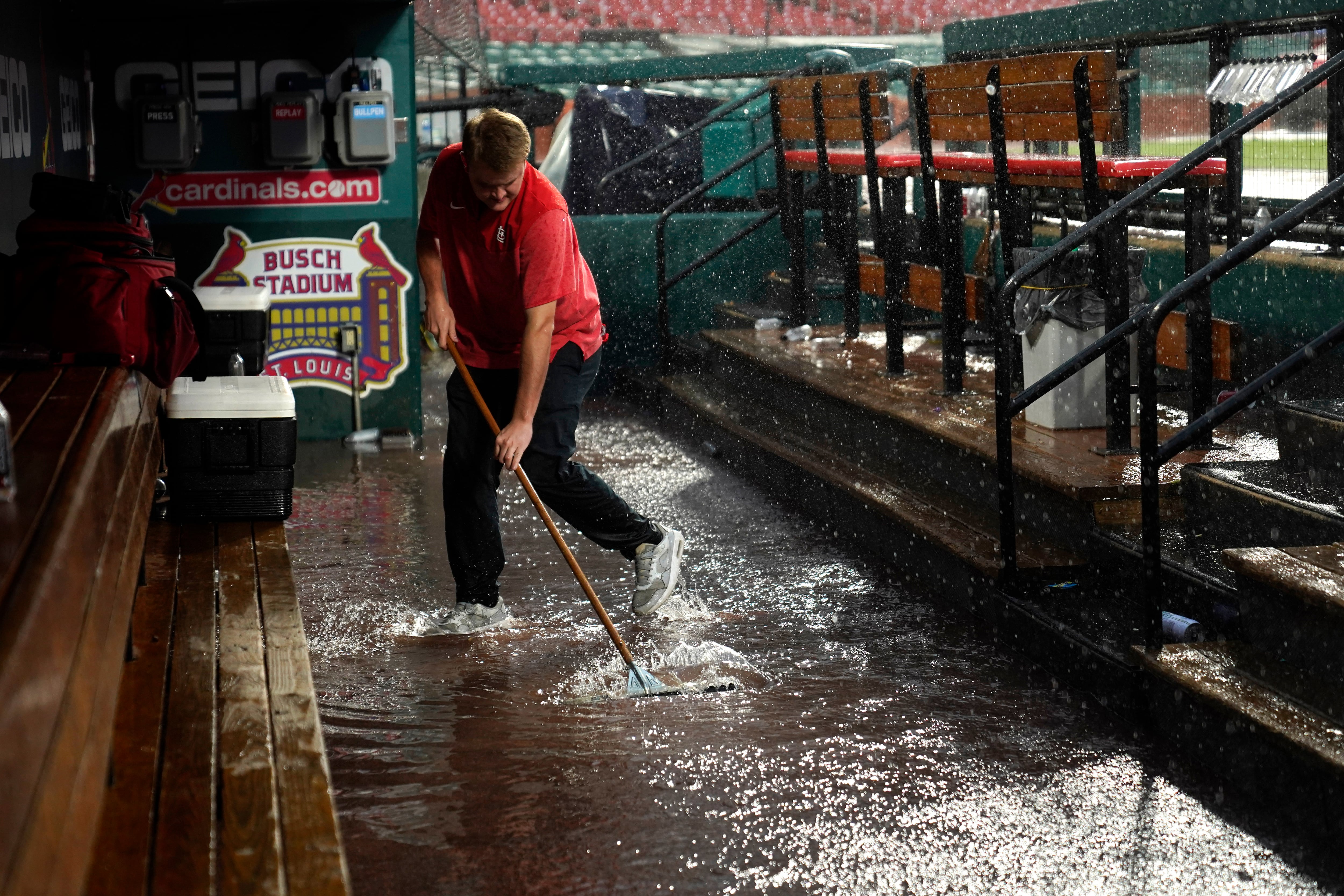 El asistente de la casa club de los St. Louis Cardinals, Andrew Rettig, intenta despejar un desagüe en el dugout inundado de los Cardinals durante un retraso por lluvia en el primer juego de una doble cartelera de béisbol entre los Cardinals y los New York Yankees