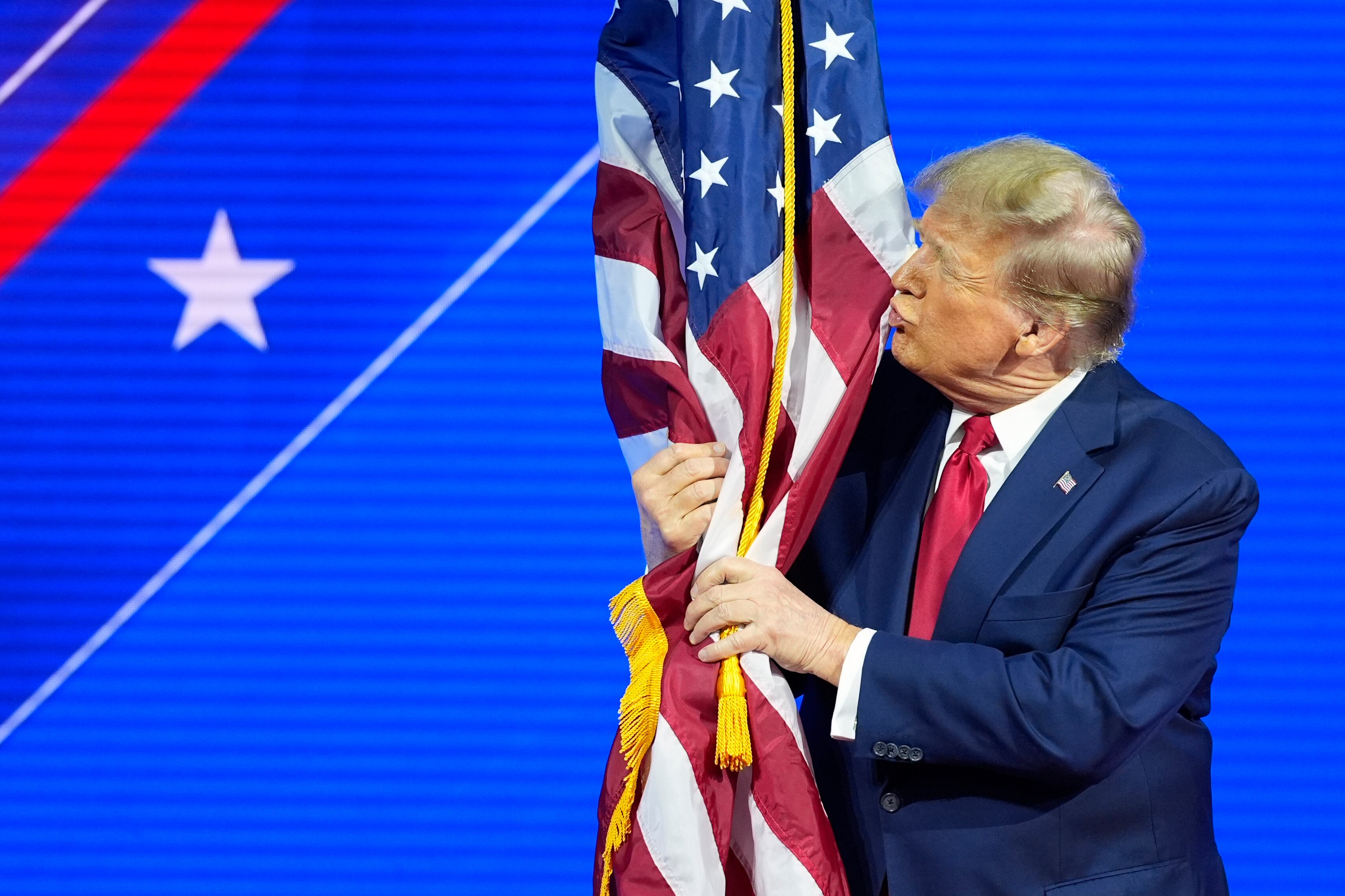 El candidato presidencial republicano, el expresidente Donald Trump, abraza y besa la bandera estadounidense mientras habla en la Conferencia de Acción Política Conservadora, CPAC.