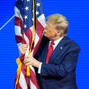 El candidato presidencial republicano, el expresidente Donald Trump, abraza y besa la bandera estadounidense mientras habla en la Conferencia de Acción Política Conservadora, CPAC.