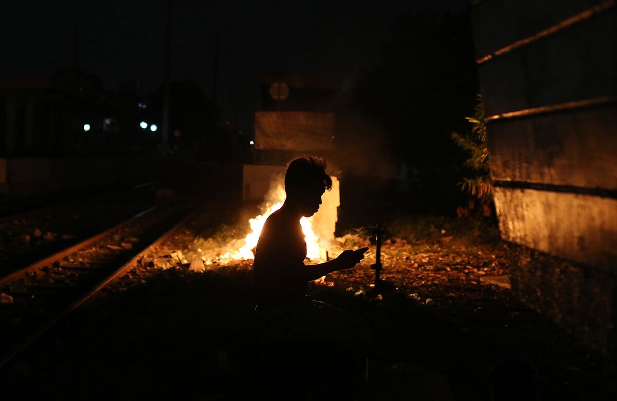 Juanito Bandong usa su smartphone junto a una fogata en las vías del tren de Manila en donde vive y trabaja, Filipinas. (AP/Aaron Favila)