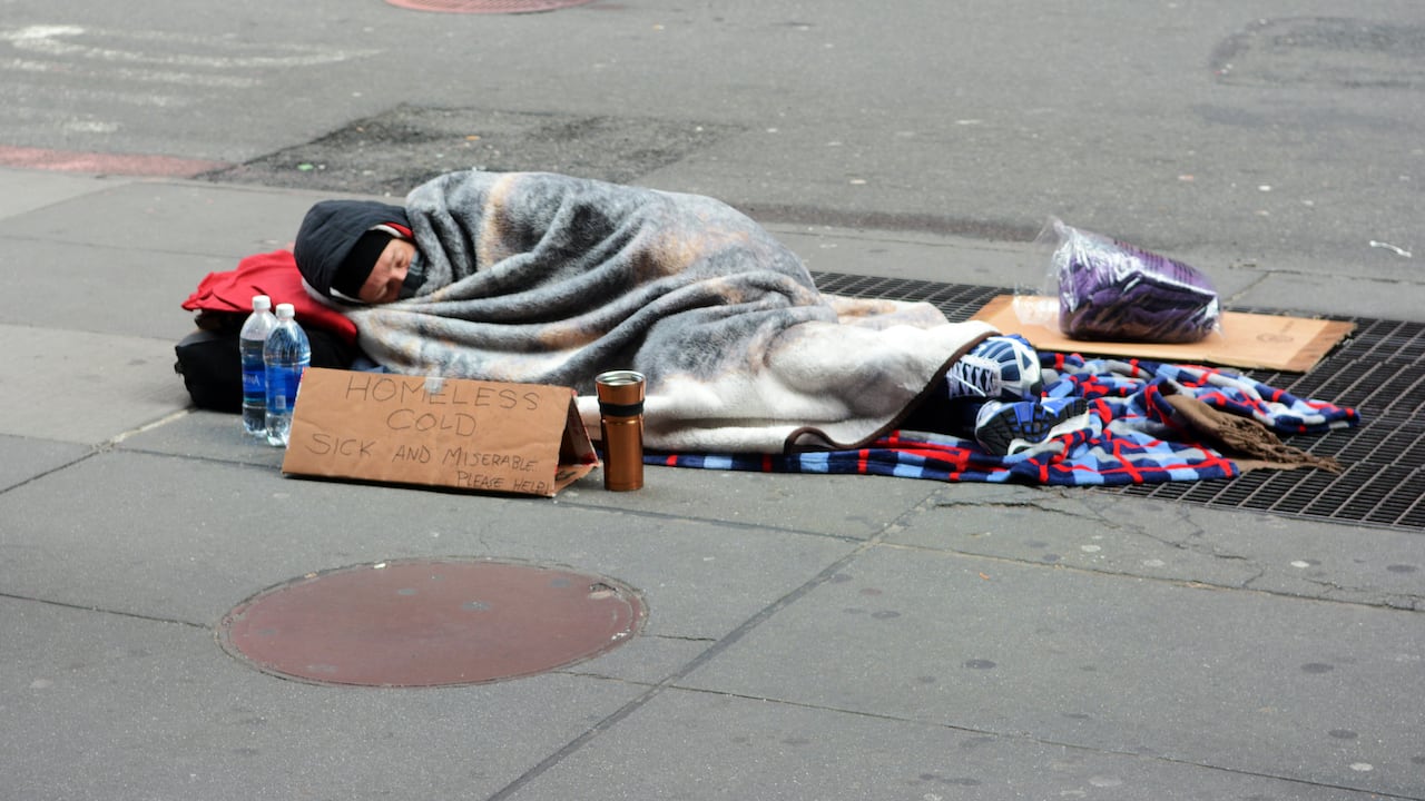 Un hombre sin hogar, con frío, enfermo y miserable, durmiendo en una acera.