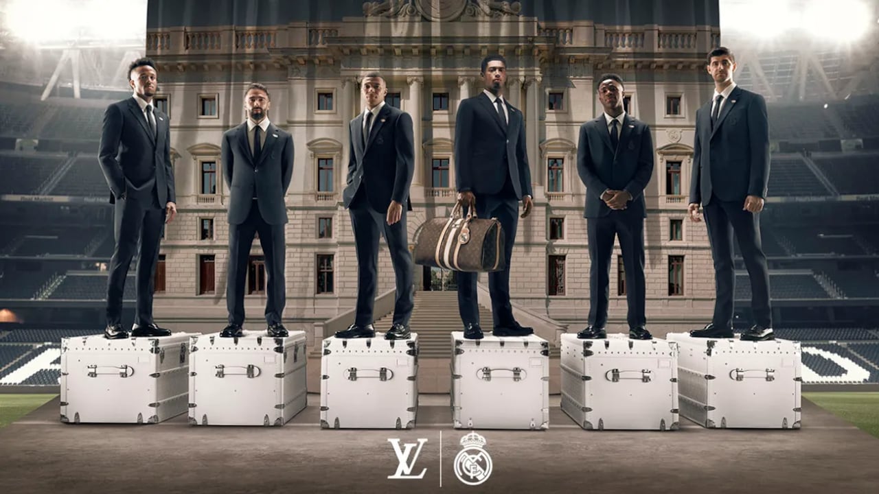Éder Militão, Daniel Carvajal, Kylian Mbappé, Jude Bellingham, Vinicius Júnior y Thibaut Courtois de pie sobre baúles Louis Vuitton, vistiendo la colección de ropa formal LV x Real Madrid.