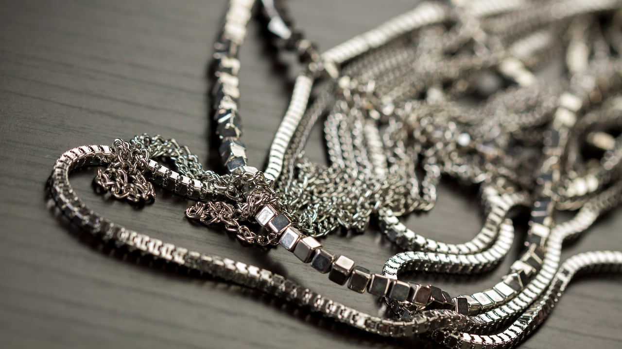 Assorted silver costume jewellery with a jumbled pile of chains with different shaped links, a clear crystal bead and a necklace of round silver beads with focus to the chains