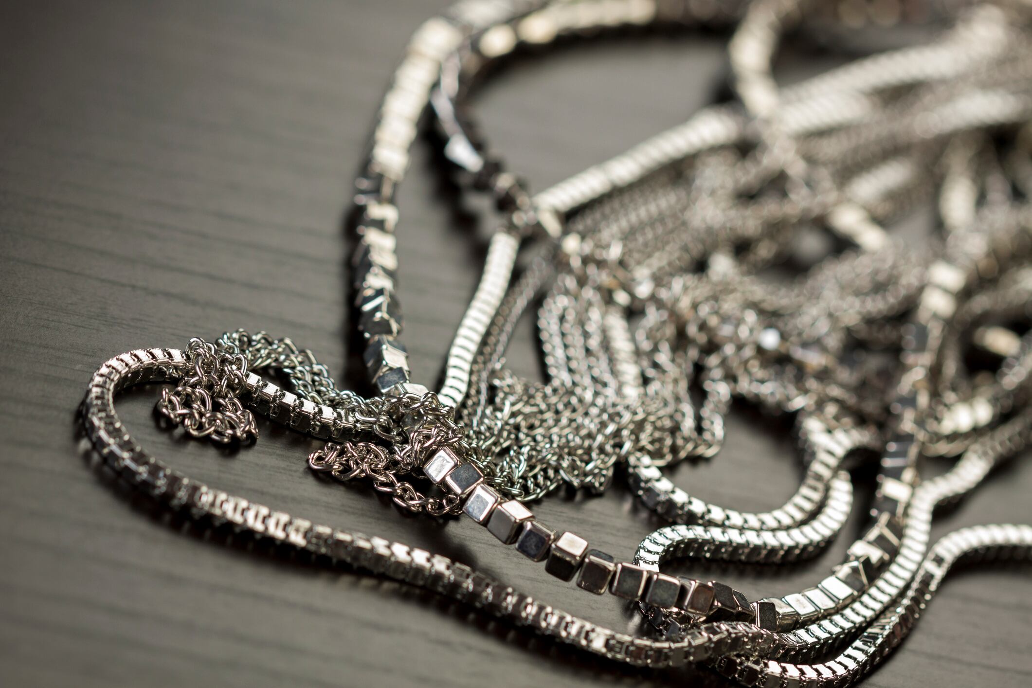 Assorted silver costume jewellery with a jumbled pile of chains with different shaped links, a clear crystal bead and a necklace of round silver beads with focus to the chains