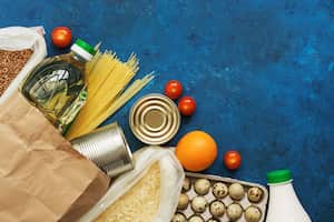 Entrega de comida a domicilio. Aceite en botella, pasta, conservas, cereales, huevos, leche, frutas y verduras sobre un fondo rústico azul. Donación y caridad. Vista superior, endecha plana, espacio de copia