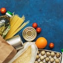 Entrega de comida a domicilio. Aceite en botella, pasta, conservas, cereales, huevos, leche, frutas y verduras sobre un fondo rústico azul. Donación y caridad. Vista superior, endecha plana, espacio de copia