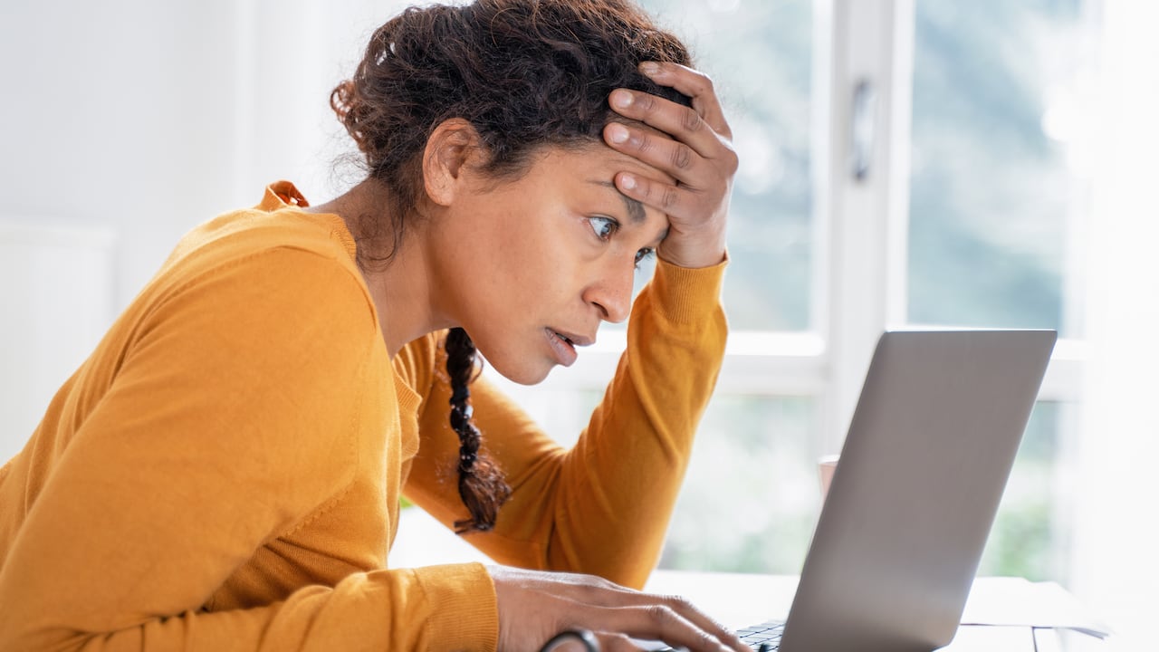 Close up color image depicting a mid adult man checking his groceries bill in the supermarket after making his purchases at the checkout. Focus on the man with the supermarket checkout defocused in the background. The man is wearing a casual blue polo shirt and has a worried expression on his face.