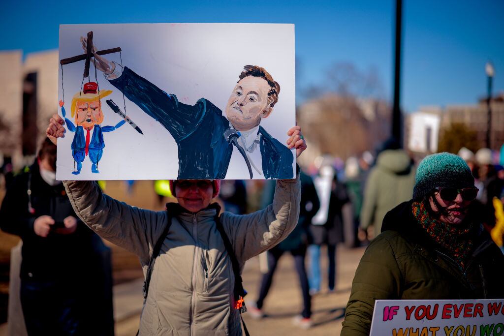WASHINGTON, DC - FEBRUARY 17: A sign depicting Tesla and SpaceX CEO Elon Musk and U.S. President Donald Trump is visible as protesters rally against the Trump administration during "Not My President's Day" protests at the Capitol Reflecting Pool on February 17, 2025 in Washington, DC. Protests are being held in cities across the nation on Presidents' Day against what the organizers say are "the anti-democratic and illegal actions of the Trump administration." (Photo by Chip Somodevilla/Getty Images)