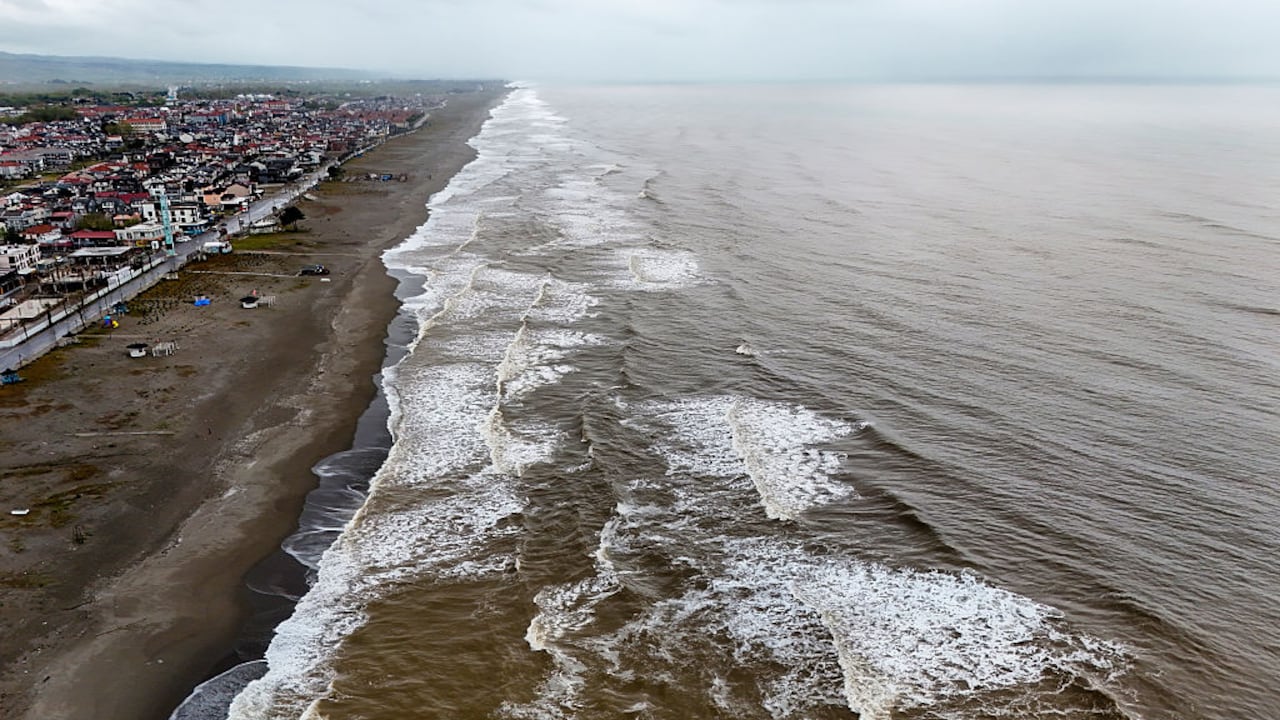 Una toma aérea de viviendas muy cerca del mar con olas entrando a las calles.