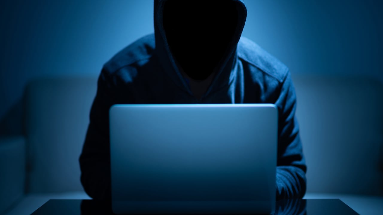Cara oscura del hacker que usa la computadora portátil en el cuarto oscuro