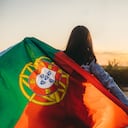 Mujer joven extendiendo la bandera portuguesa al aire libre, mientras el sol se pone.