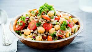 Una ensalada de garbanzos y cuscús perla mezclada con tomates, cebollas y hierbas.