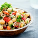Una ensalada de garbanzos y cuscús perla mezclada con tomates, cebollas y hierbas.
