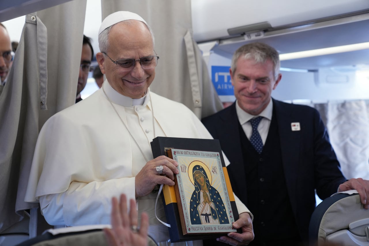 Pope Leo XIV holds an icon as he greets reporters aboard a flight on his way to Ankara on November 27, 2025. Pope Leo XIV arrived in Turkey on the first overseas trip of his papacy, which will also take him to Lebanon. (Photo by Domenico Stinellis / POOL / AFP)