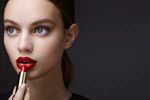 Foto de estudio de una hermosa joven morena con un lápiz labial rojo en la mano delante de un fondo oscuro