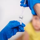 Médico con guantes protectores llenando una jeringa de inyección con la vacuna COVID-19 y listo para administrar la vacuna Covid-19 a una niña.