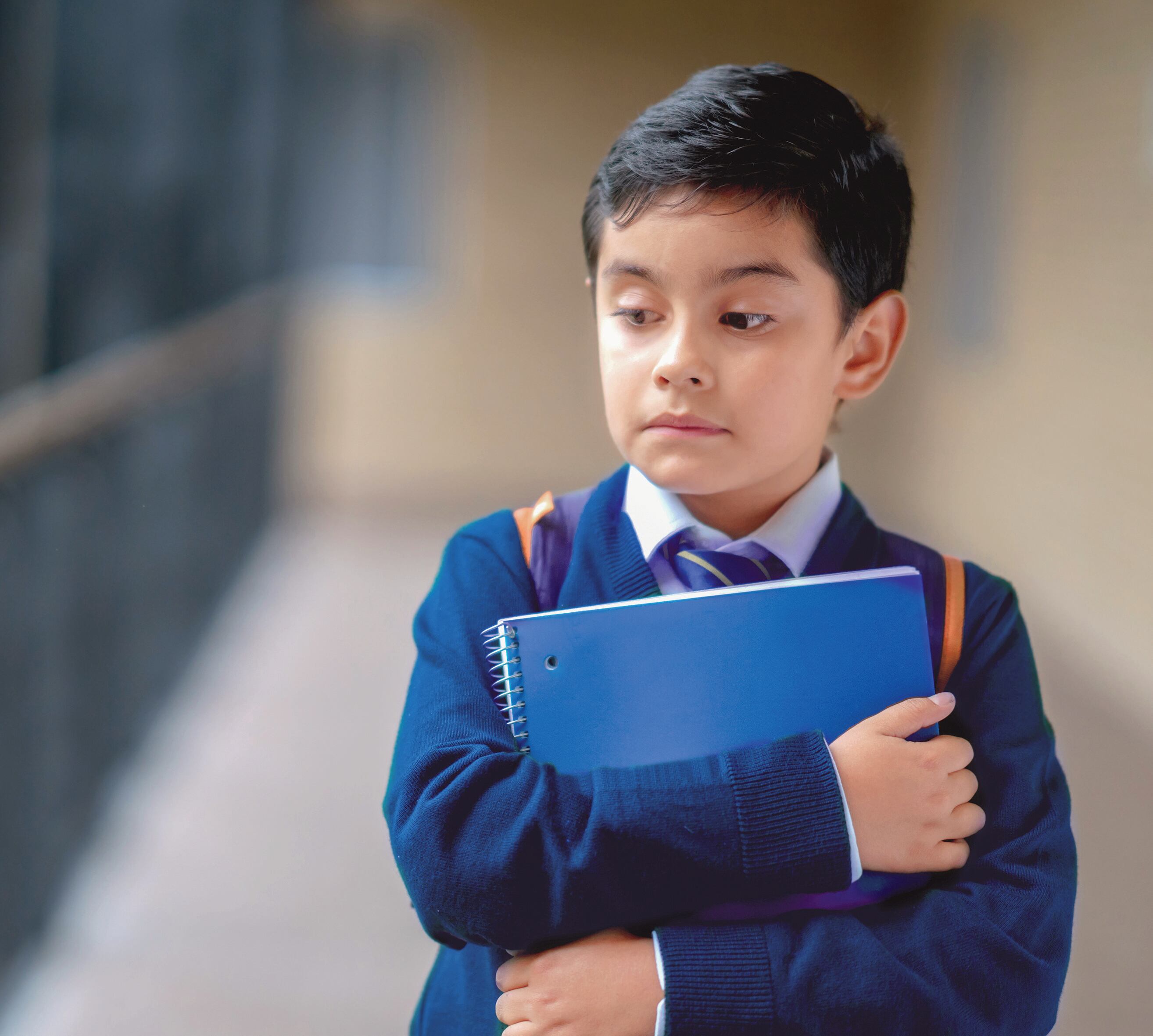 Sad boy at school walking in the hallway holding a notebook - education concepts