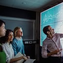 Grupo de profesionales de negocios en una habitación oscura parados frente a una gran pantalla de visualización de datos con información.