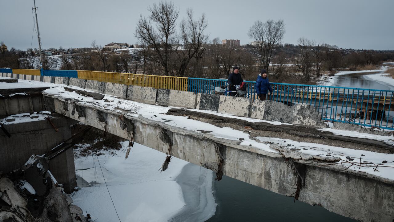 Elena (derecha) y Petr cruzan un puente destruido después de recolectar agua potable de un punto de distribución en Kupiansk el 13 de febrero de 2023, en medio de la invasión rusa de Ucrania. (Foto de YASUYOSHI CHIBA / AFP)