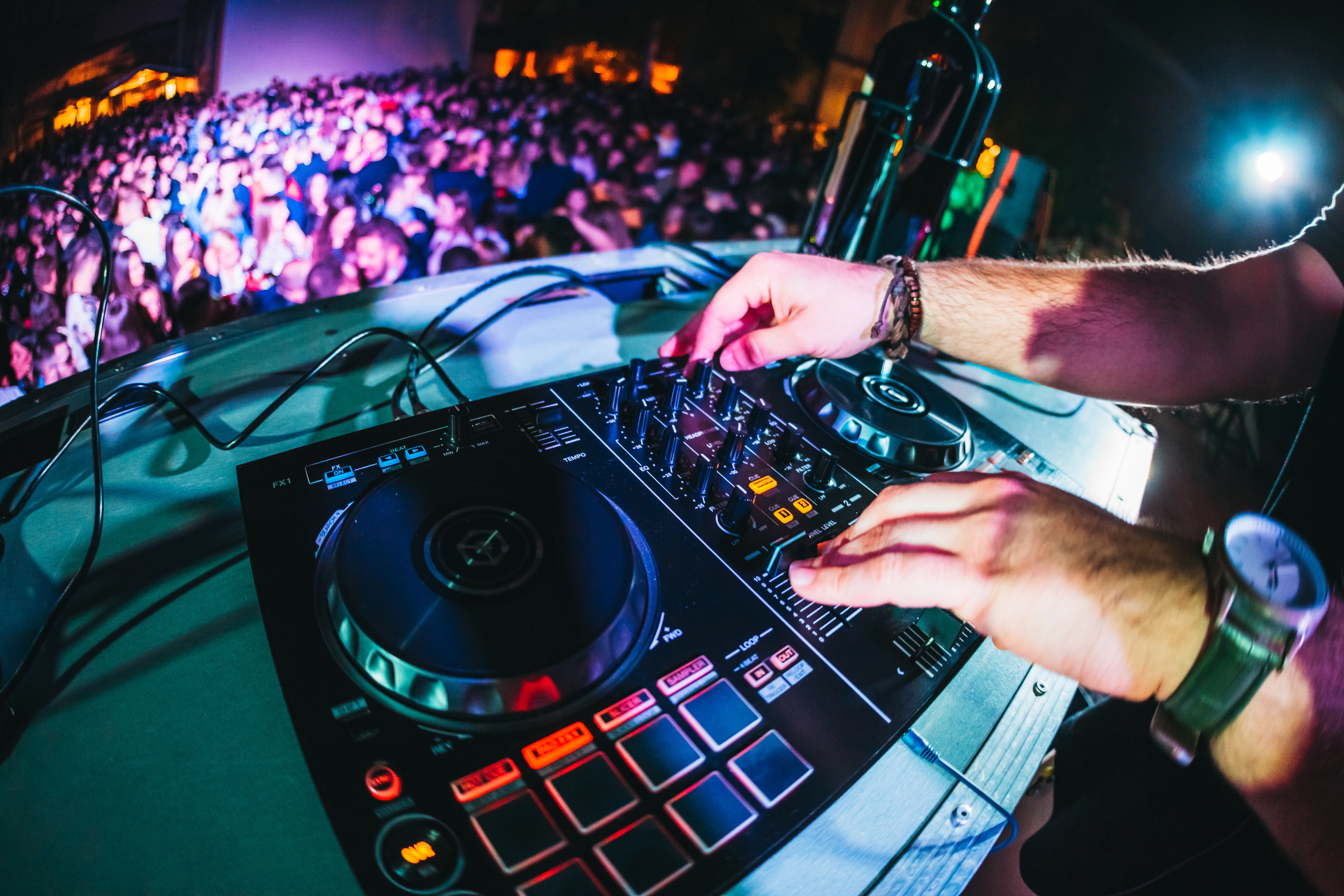 Club, disco DJ playing and mixing music for crowd of happy people. Nightlife, concert lights, flares.