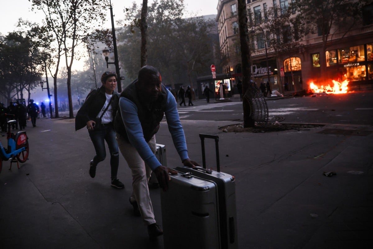 Turistas corren con su equipaje cerca de la plaza de La Madeleine, donde se observa un incendio durante una manifestación contra el «alto costo de la vida» en París, el 17 de octubre de 2026