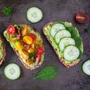 Surtido de tostadas de aguacate saludables. Huevos, tomates y pepino espinaca. Lay Flat sobre un fondo oscuro.