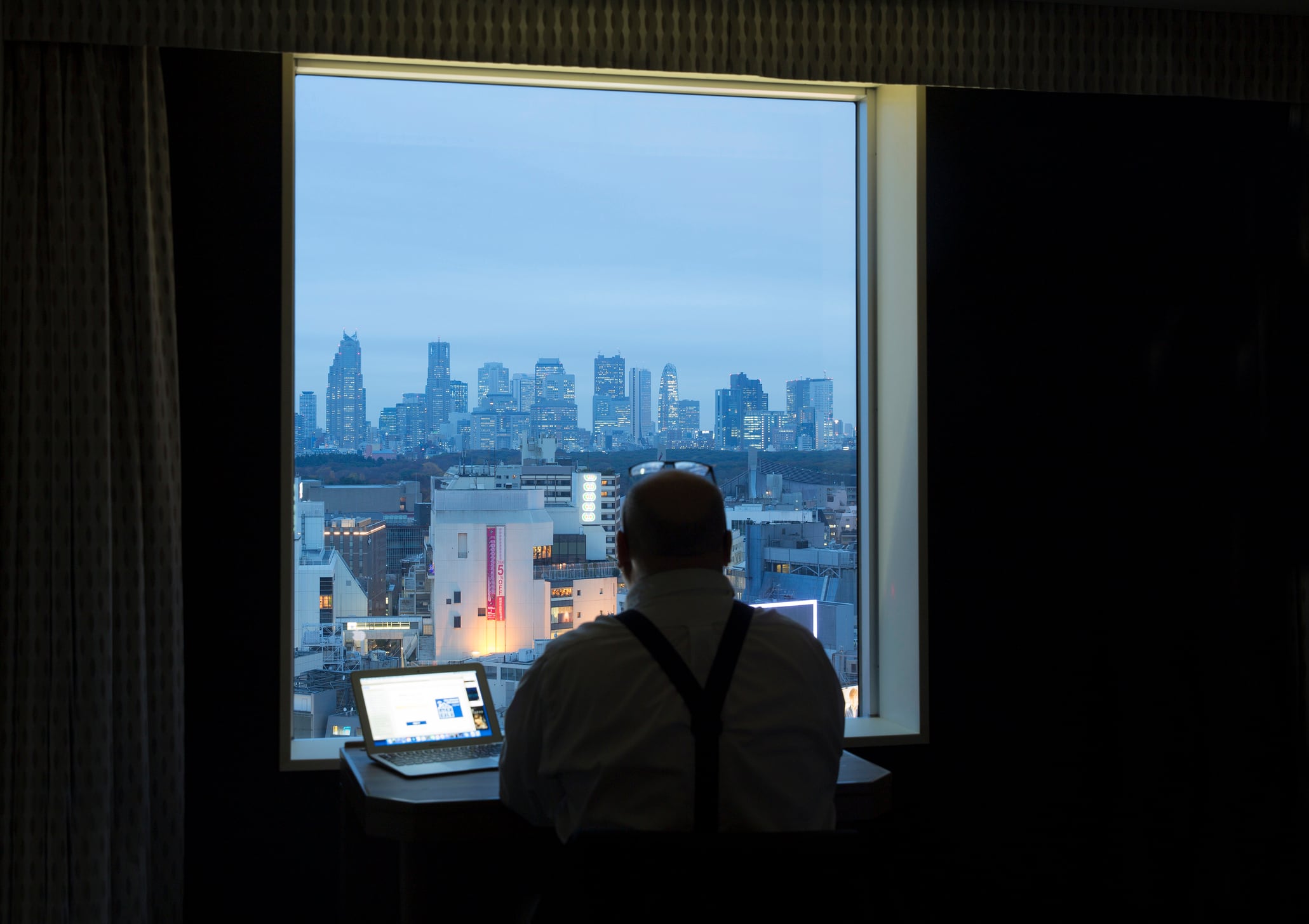 Man looking out of hotel window at Shinjuku business district
