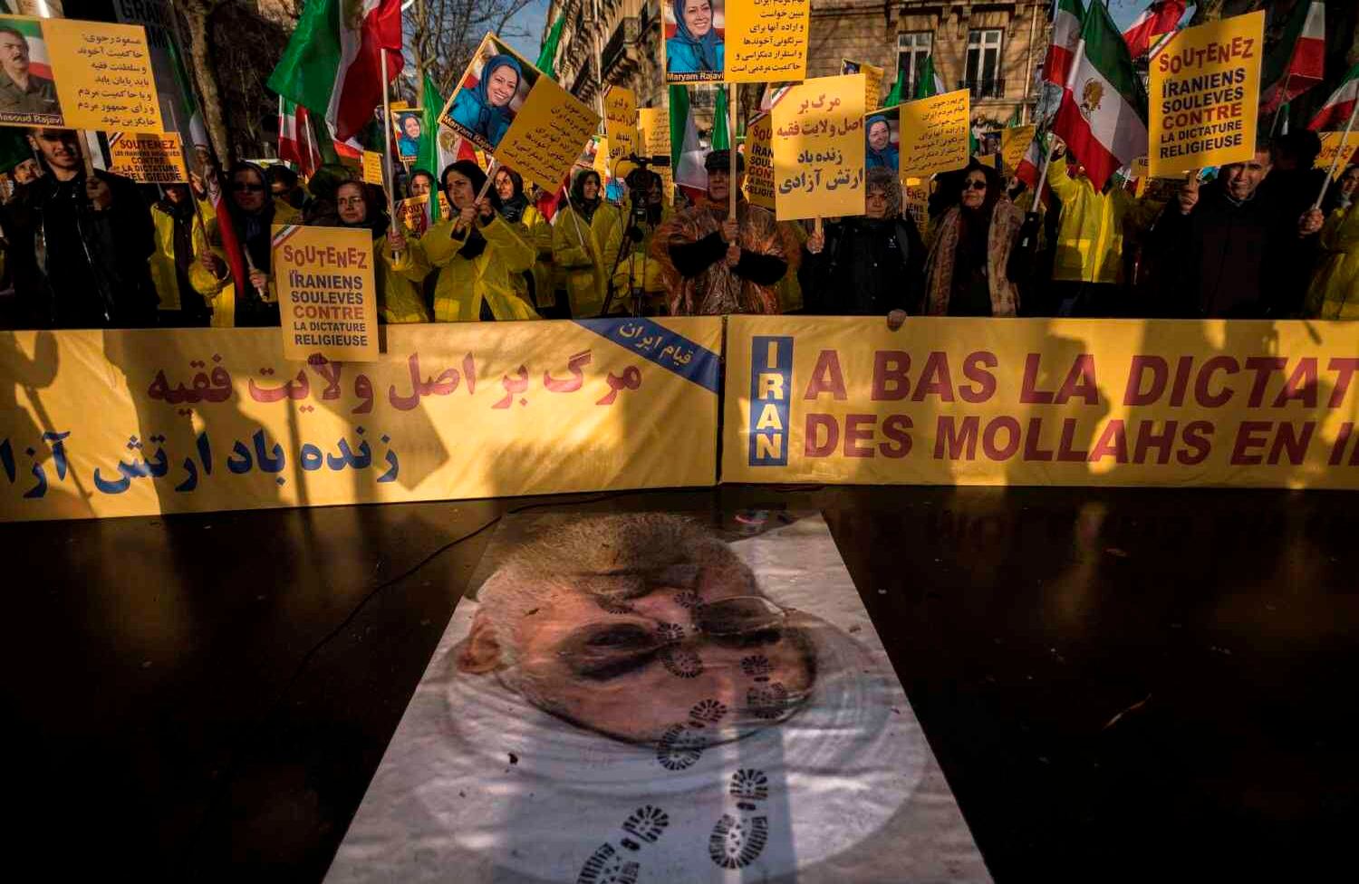 Manifestantes sostienen pancartas que dicen "Apoye a los iraníes levantados contra la dictadura religiosa" mientras respaldan un retrato del presidente iraní Hassan Rouhani con marcas de zapatos durante una manifestación en apoyo del pueblo iraní en medio de una ola de protestas que se extienden por todo Irán, la manifestación fue en París./ AFP PHOTO / Lionel BONAVENTURE