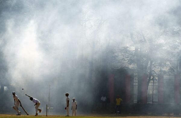 Algunos niños juegan cricket entre el humo que generó la fumigación para evitar la malaria en Mumbai, India. (AP)