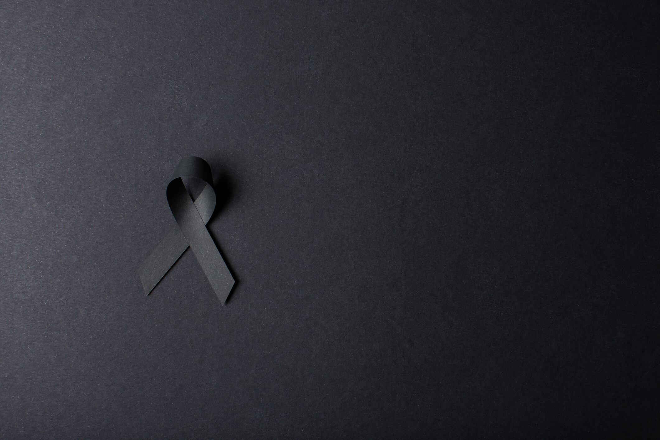 Black handmade awareness paper ribbon on black background.