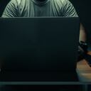 A man in a white shirt sits on a laptop in a dark room. with light shining down. internet concept addiction.topview.