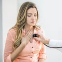 Mujer joven a la que un médico le examina el pecho doloroso.