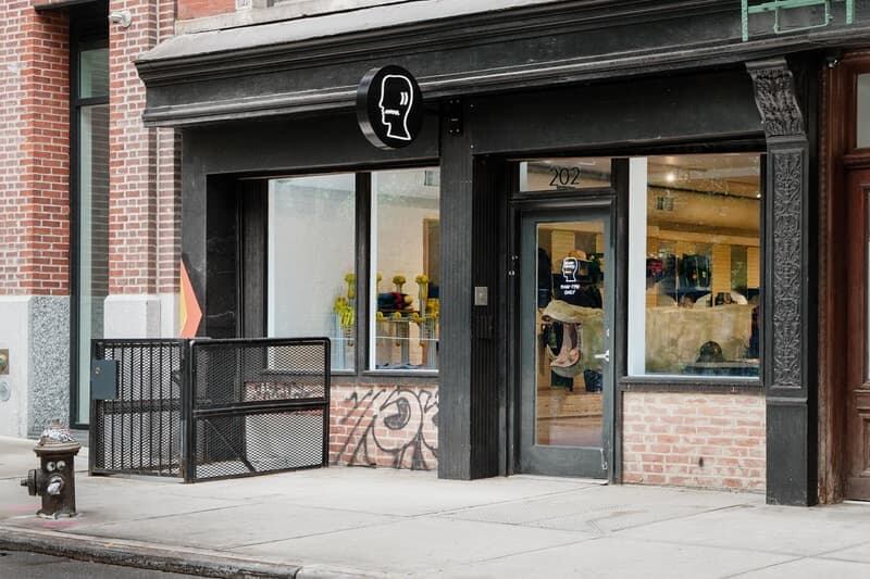 Exterior de la tienda Brain Dead en Nueva York mostrando productos de streetwear, decoración artística y una escultura central en un espacio moderno e industrial.