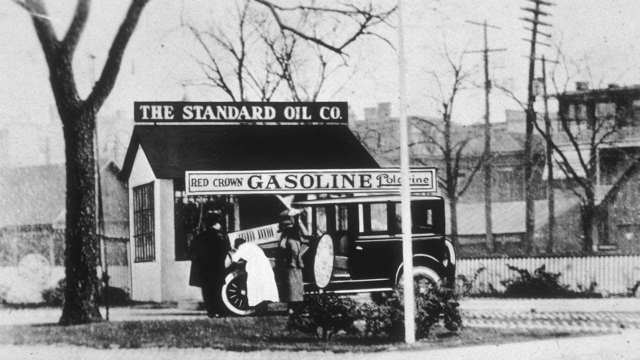 circa 1918: Three people look under the hood of an automobile in front of a Standard Oil gas station. (Photo by Hulton Archive/Getty Images)