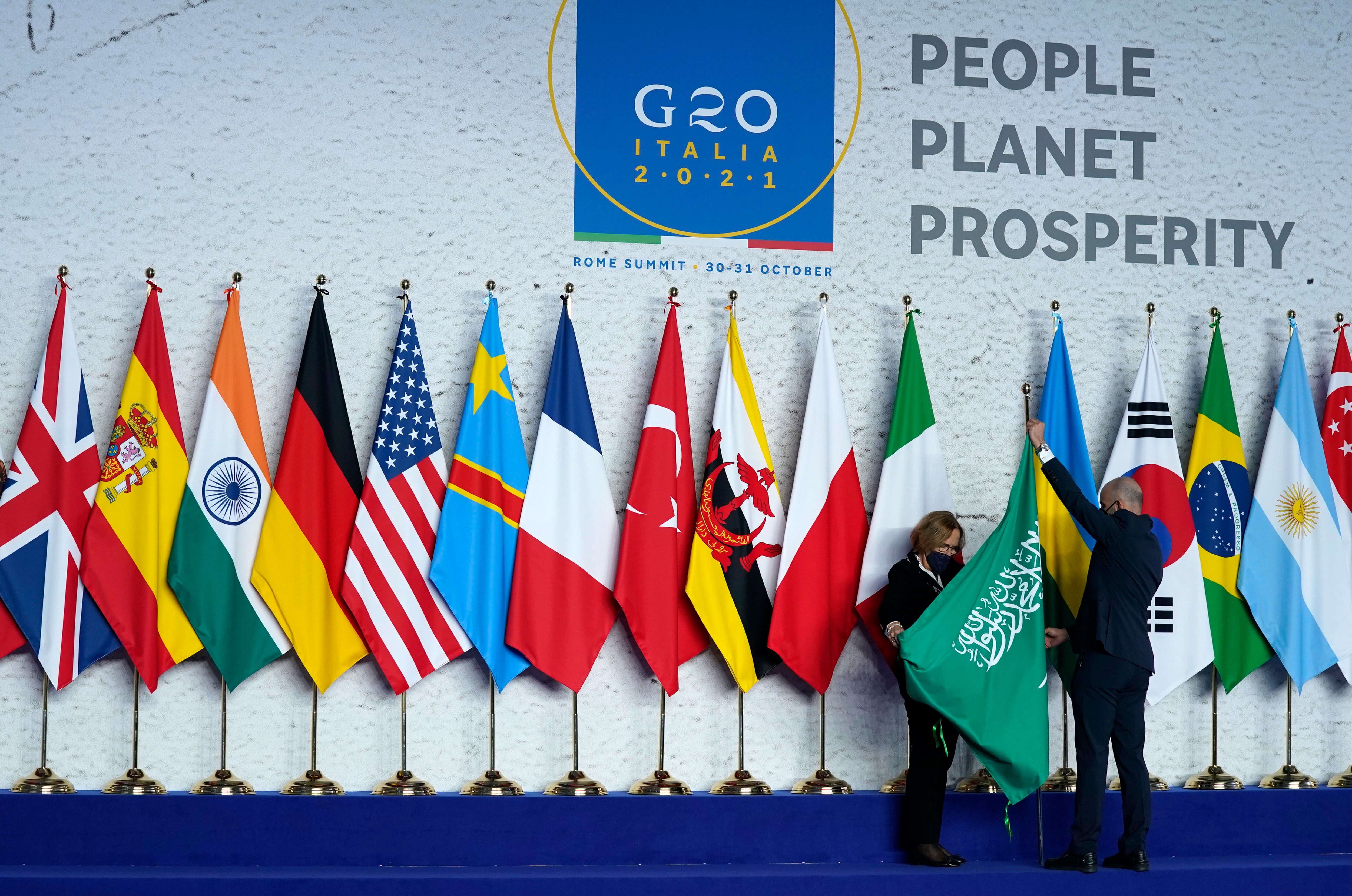 Operarios ajustan la bandera de Arabia Saudí antes de una foto grupal al inicio de la cumbre del G20 en Roma, el 30 de octubre de 2021. (AP Foto/Evan Vucci, Pool)