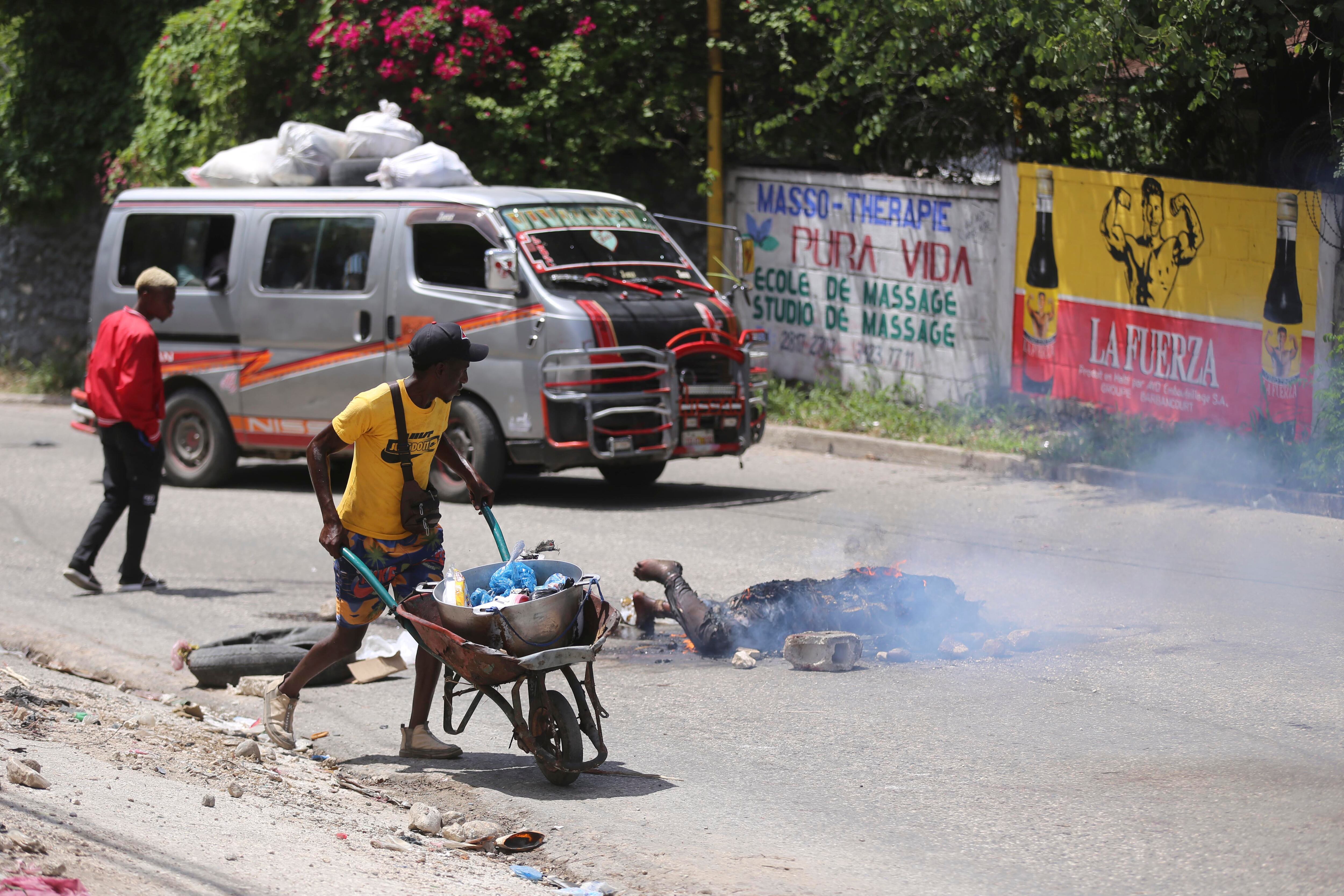 La gente pasa junto al cuerpo de un hombre acusado de robar una motocicleta que fue asesinado e incendiado en el barrio de Petion-ville de Port-au-Prince, Haití