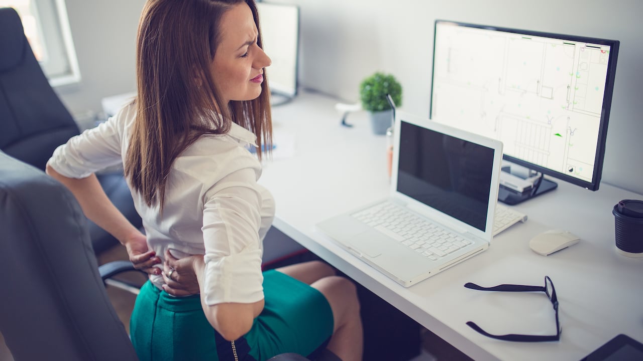 Young woman having back pain while sitting at desk in office