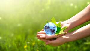 Environment Day concept. Earth crystal glass globe ball and maple leaf in human hand on grass background. Saving environment, save clean green planet, ecology theme. Card for World Earth Day.
