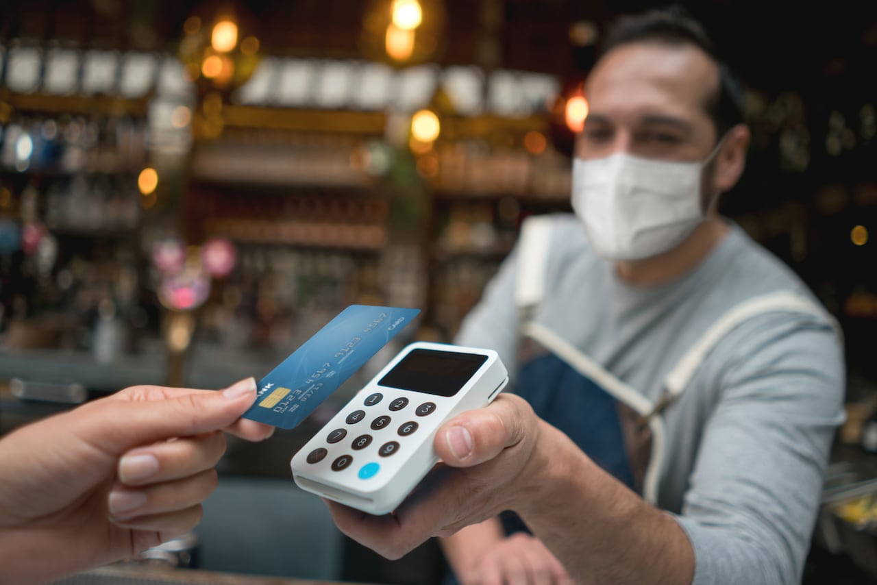 Mesero con mascarilla mientras recibe un pago sin contacto en un restaurante: conceptos de estilo de vida COVID-19. ** EL DISEÑO DE LA TARJETA DE CRÉDITO FUE HECHO A PARTIR DE NOSOTROS **
