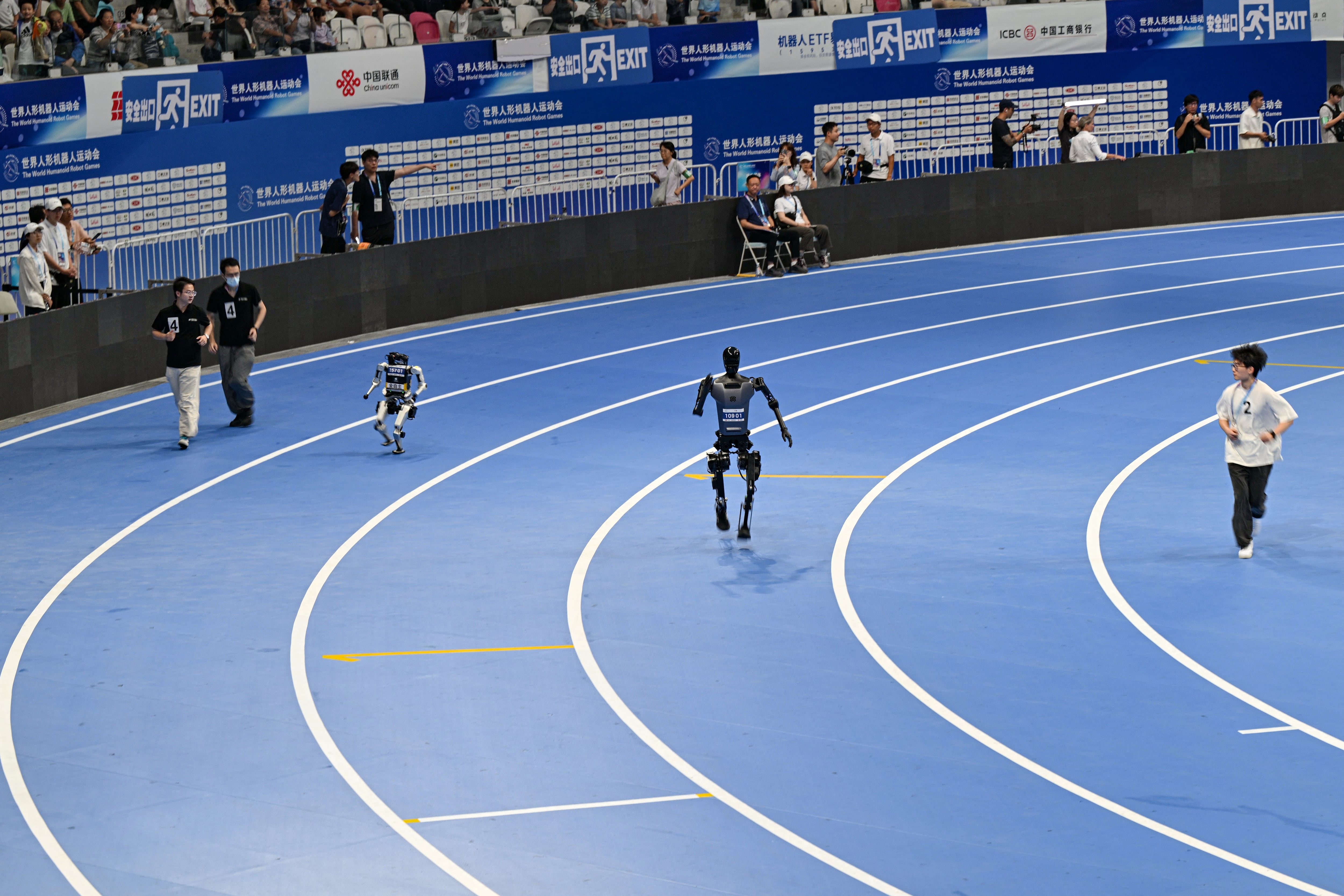 Los ingenieros siguen a sus robots mientras compiten en la carrera de 400 metros durante los Juegos Mundiales de Robots Humanoides en Beijing el 15 de agosto de 2025. (Foto de ADEK BERRY / AFP)
