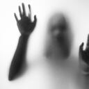 Horror woman behind the matte glass in black and white. Blurry hand and body figure abstraction.Halloween background