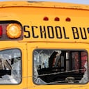 A close-up of the rear of an old school bus with broken windows and rusting paint.