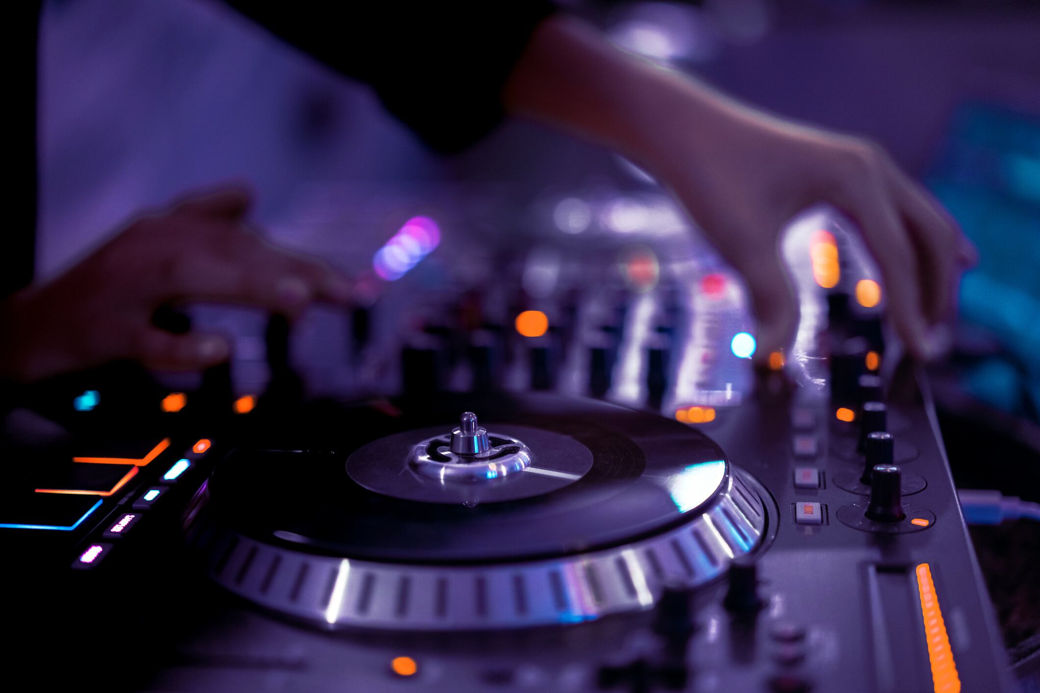 Close-up of an American DJ, working with sound, adjusting basses and high tones, spinning turntable records at a night club party in purple and very peri neon lights. Musical apps and podcasts concept