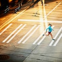 Pregnant woman running across sidewalk during early morning run on empty city street