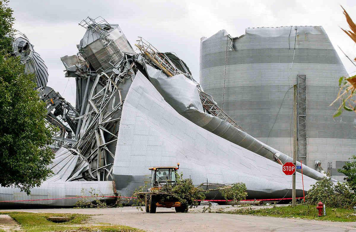 Los trabajadores del Departamento de Transporte de Iowa ayudan con la remoción de los escombros de árboles. También se observa el daño en varios contenedores de granos de la instalación de Archer Daniels Midland por culpa de la tormenta que el lunes azotó el Medio Oeste con vientos en línea recta de hasta 100 millas por hora. La tormenta ganó fuerza a medida que avanzaba a través de los campos agrícolas de Iowa, aplanando el maíz y reventando los contenedores de granos aún llenos de decenas de millones de bushels de la cosecha del año pasado. Foto: Jim Slosiarek / The Gazette vía AP