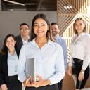 Confident hispanic businesswoman standing in office with colleagues in background