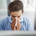 Foto de un joven empresario sonándose la nariz con un pañuelo en el trabajo