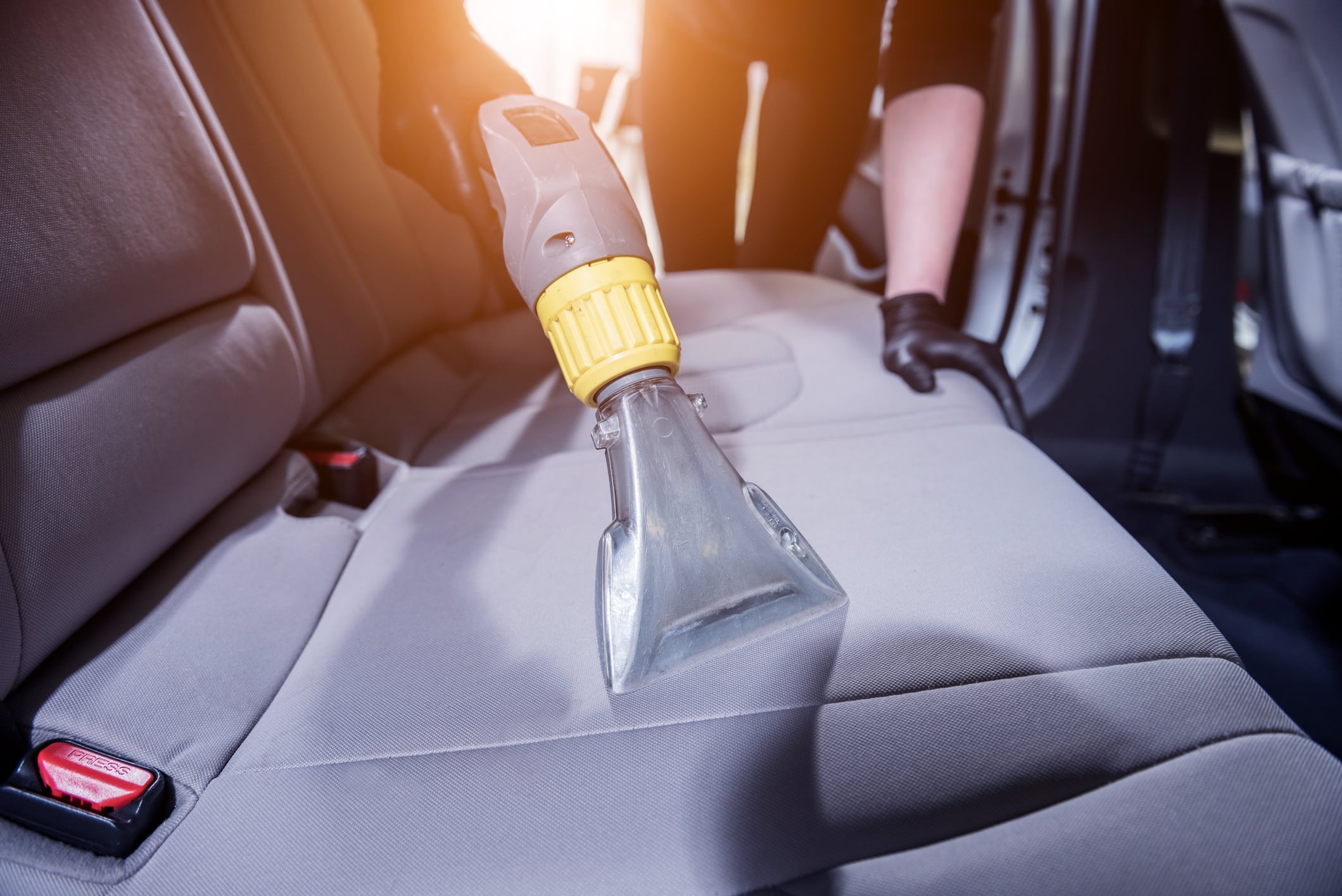 Worker cleans car interior with vacuum cleaner.