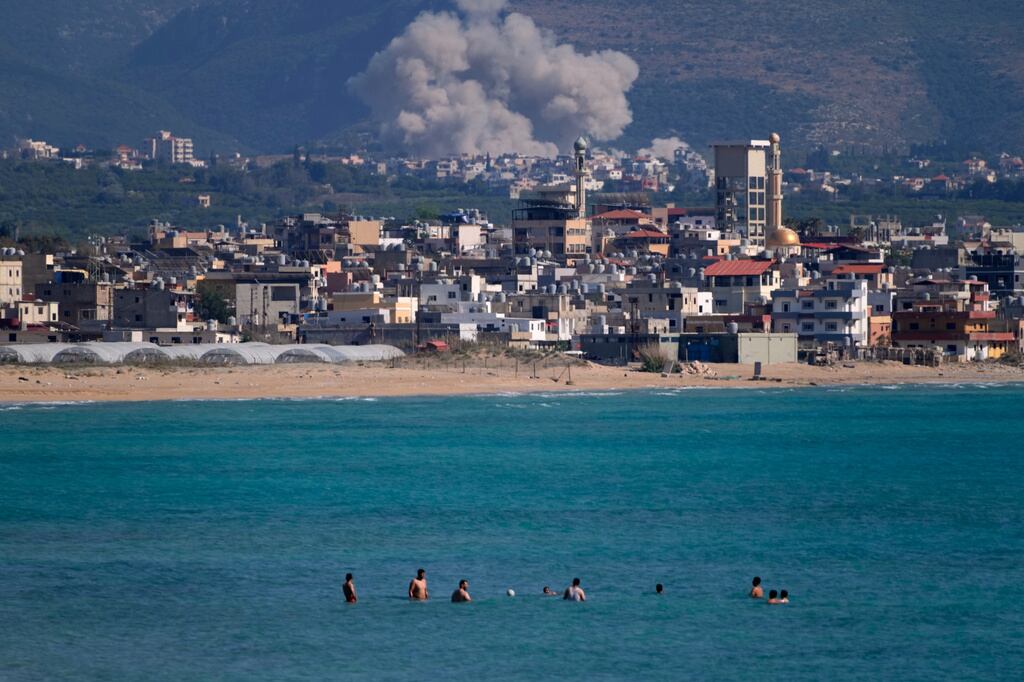 Unas personas nadan en una playa pública mientras al fondo se ve humo tras un ataque aéreo israelí que impactó la aldea de Qlaileh, vista desde Tiro, Líbano, el 2 de junio de 2026. (AP Foto/Mohammed Zaatari)