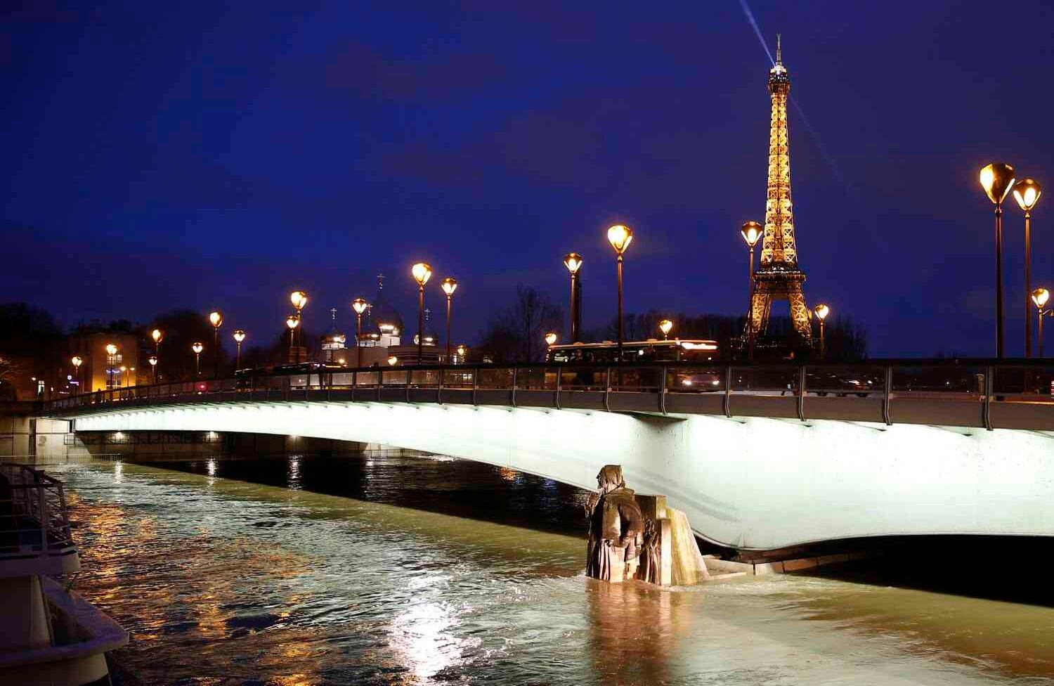 La torre Eiffel iluminada, junto al río Sena, con niveles de agua elevados a la altura de la estatua Zouave del puente Pont d'Alma. El Sena siguió en aumento inundando las calles y colocando a los museos en una situación de emergencia. / AFP PHOTO / Geoffroy Van Der Hasselt.